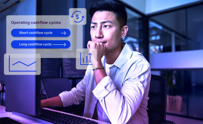 A young man in a white shirt sits at a desk, looking thoughtfully at a computer. The modern office has glass walls and multiple monitors. A blue-tinted overlay features 'Operating cashflow cycles' with buttons for 'Short cashflow cycle' and 'Long cashflow cycle,' along with icons of a dollar sign and a bar chart.